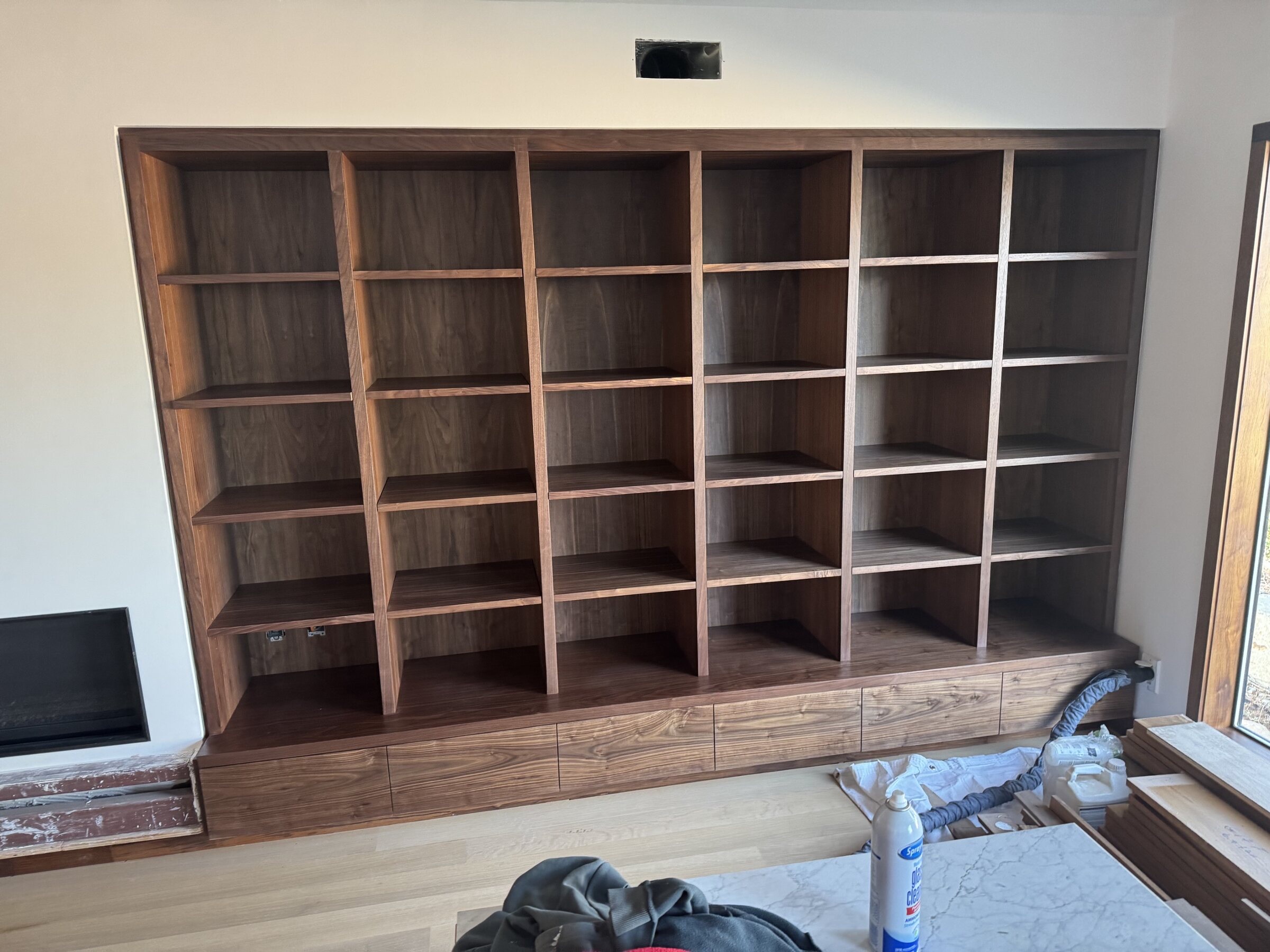 Large walnut grid built-in with open cubbies and base drawers beside a fireplace